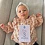 Esmée participe au concours pour gagner de l'argent avec cette photo : baby, infant, milestone_card, floral_clothing, head_wrap, couch, gray_couch, milestone, card, person, child, indoors, cute, portrait, laying_down, expressive_face, pink, black_pants, fabric, home