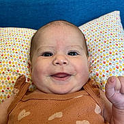 Esmée participe au concours pour gagner de l'argent avec cette photo : baby, smiling, infant, face, clothing, pillow, pattern, heart, brown, blue, happy, cute, skin, person, portrait, indoors, closeup, child, young, sitting