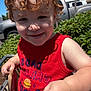 toddler, child, curly_hair, shopping_cart, red_tank_top, outdoor, sunny_day, greenery, car_keys, smiling, face, hand, clothing, casual, blue_sky, vehicle, plant, shadow, holding, cute