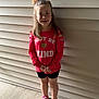 child, girl, smiling, red_shirt, bow, standing, outside, concrete, sneakers, shorts, wall, beige, hair, happy, casual_clothing, portrait, person, footwear, positive_message, daylight