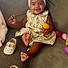 accessory, baby, celebration, child, colorful, couch, cute, dress, easter_egg, foot, happy, headband, indoors, infant, person, playful, shoe, sitting, smiling, toy