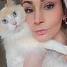 woman, cat, selfie, close_up, blue_eyes, fluffy, cream_colored, face, portrait, makeup, pout, earrings, bracelet, indoor, light_skin, long_hair, pet, cute, holding, curious