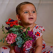 Chloé participe au concours pour gagner de l'argent avec cette photo : background, blue_eyes, bouquet, child, cute, dress, expression, floral_pattern, flowers, greenery, indoor, person, pink_flowers, portrait, purple_flowers, red_flowers, sitting, soft_lighting, toddler, vase
