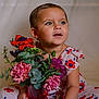 background, blue_eyes, bouquet, child, cute, dress, expression, floral_pattern, flowers, greenery, indoor, person, pink_flowers, portrait, purple_flowers, red_flowers, sitting, soft_lighting, toddler, vase