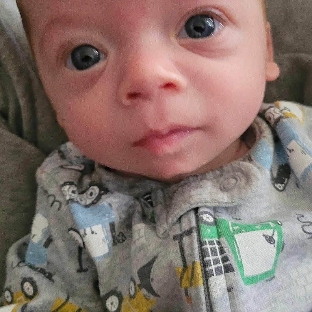 Maverick is registered to the contest to win money with this photo: baby, infant, face, eyes, onesie, clothing, cute, portrait, child, newborn, expression, skin, person, young, closeup, indoors, casual, head, looking, adorable