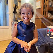 Aliyah participe au concours pour gagner de l'argent avec cette photo : blurred_background, cabinet, casual, child, clothing, curly_hair, dress, face, floor, furniture, hands, happy, home, indoor, person, portrait, room, smiling, table, young_child