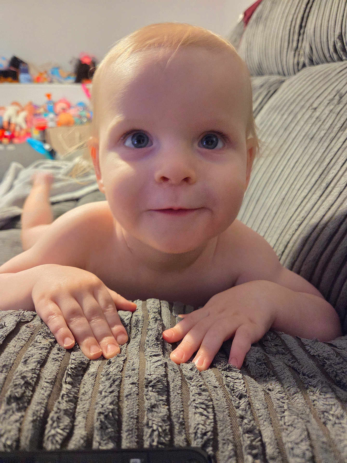 Kai is registered to the contest to win money with this photo: baby, child, face, hands, couch, texture, indoor, curious, smile, blue_eyes, skin, person, infant, furniture, toy, blurred_background, close_up, home, laying, young