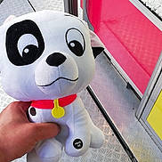 Orka participe au concours pour gagner de l'argent avec cette photo : plush_toy, dog, hand, red_collar, button, press_me, metal_floor, cartoon_eyes, white, black_spot, pink_ears, yellow_tag, background_panels, colorful, indoor, toy, soft, cute, playful, stuffed_animal