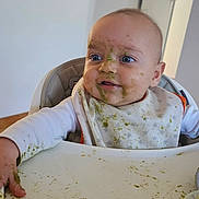 Kayden a rejoint le concours — aidez-le/la à gagner de superbes lots ! baby, high_chair, messy, food, bib, face, blue_eyes, clothing, indoor, child, feeding, green_food, hand, table, expression, person, smudge, curious, sitting, toddler