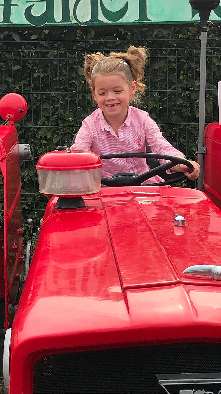 Lola participe au concours pour gagner de l'argent avec cette photo : automotive_design, automotive_exterior, automotive_window_part, bumper, child, classic, grass, hood, joy, leisure, magenta, motor_vehicle, person, pink, recreation, red, riding_toy, smile, toddler, tractor