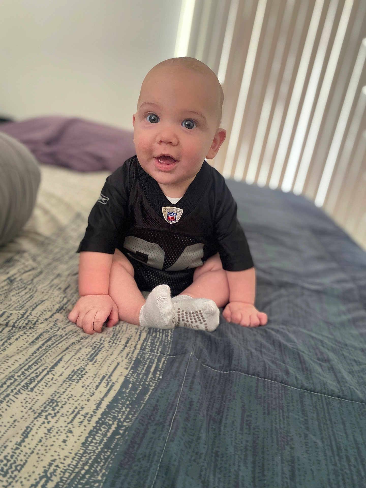 Lorenzo is registered to the contest to win money with this photo: baby, infant, child, bed, blanket, clothing, socks, person, portrait, indoors, cute, smiling, sitting, face, head, expression, young, soft_light, home, comfort
