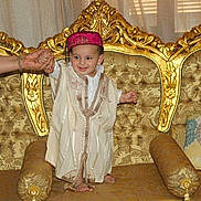 Soulayman participe au concours pour gagner de l'argent avec cette photo : toddler, child, traditional_clothing, sofa, golden, ornate, couch, smiling, hand_holding, person, indoor, home, furniture, decor, pillow, footwearless, curtain, happy, baby, portrait