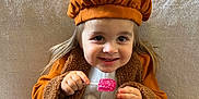 Lya a rejoint le concours — aidez-le/la à gagner de superbes lots ! child, toddler, smile, face, beret, coat, brown_coat, white_dress, lollipop, happy, cute, portrait, sitting, indoor, soft_background, long_hair, hands, playful, fashion, warm_clothing