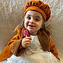 Lya a rejoint le concours — aidez-le/la à gagner de superbes lots ! toddler, child, smiling, orange_coat, hat, lollipop, white_dress, portrait, happy, cute, indoor, face, hand, clothing, texture, person, small_child, fashion, sweet, background