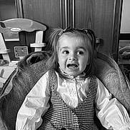 Lya a rejoint le concours — aidez-le/la à gagner de superbes lots ! toddler, child, pigtails, checkered_dress, white_shirt, smiling, indoor, chair, blanket, toy_kitchen, furniture, portrait, face, happy, young_child, casual, cozy, monochrome, expression, home