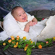 Austin is registered to the contest to win money with this photo: baby, infant, smiling, eggshell, flowers, greenery, prop, portrait, cute, happy, white_clothing, fabric, nature_theme, studio_photo, background, artificial, scene, child, nest, playful