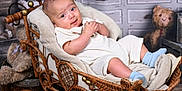 Austin is registered to the contest to win money with this photo: baby, blanket, blue_socks, child, cozy, cute, decor, furniture, indoor, infant, portrait, resting, smiling, soft_toys, teddy_bear, vintage, warm_lighting, white_clothing, wicker_carriage, wooden_floor