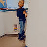 child, smiling, stairs, indoor, carpet, holding_object, braided_hair, casual_clothing, boots, young, person, wall, railing, playful, standing, beads, blue_jeans, black_top, happy, interior