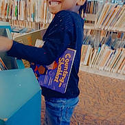 Integrity joined the competition — help win amazing prizes! child, smiling, library, books, bookshelf, indoor, person, happy, braids, long_sleeve, jeans, footwear, carpet, reading, education, young, standing, holding, cute, bright