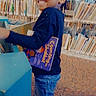 child, smiling, library, books, bookshelf, indoor, person, happy, braids, long_sleeve, jeans, footwear, carpet, reading, education, young, standing, holding, cute, bright