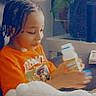 Joshua is registered to the contest to win money with this photo: child, braids, orange_shirt, stuffed_animal, bottle, plant, indoor, table, toy, person, sitting, young_child, casual_clothing, curious, cozy, home, relaxed, portrait, focus, cute