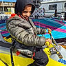 amusement_ride, blue_sky, carnival, casual_clothing, child, colorful, daylight, fun, handlebars, hoodie, jacket, outdoor, park, person, playful, recreation, seatbelt, smiling, yellow_vehicle, young