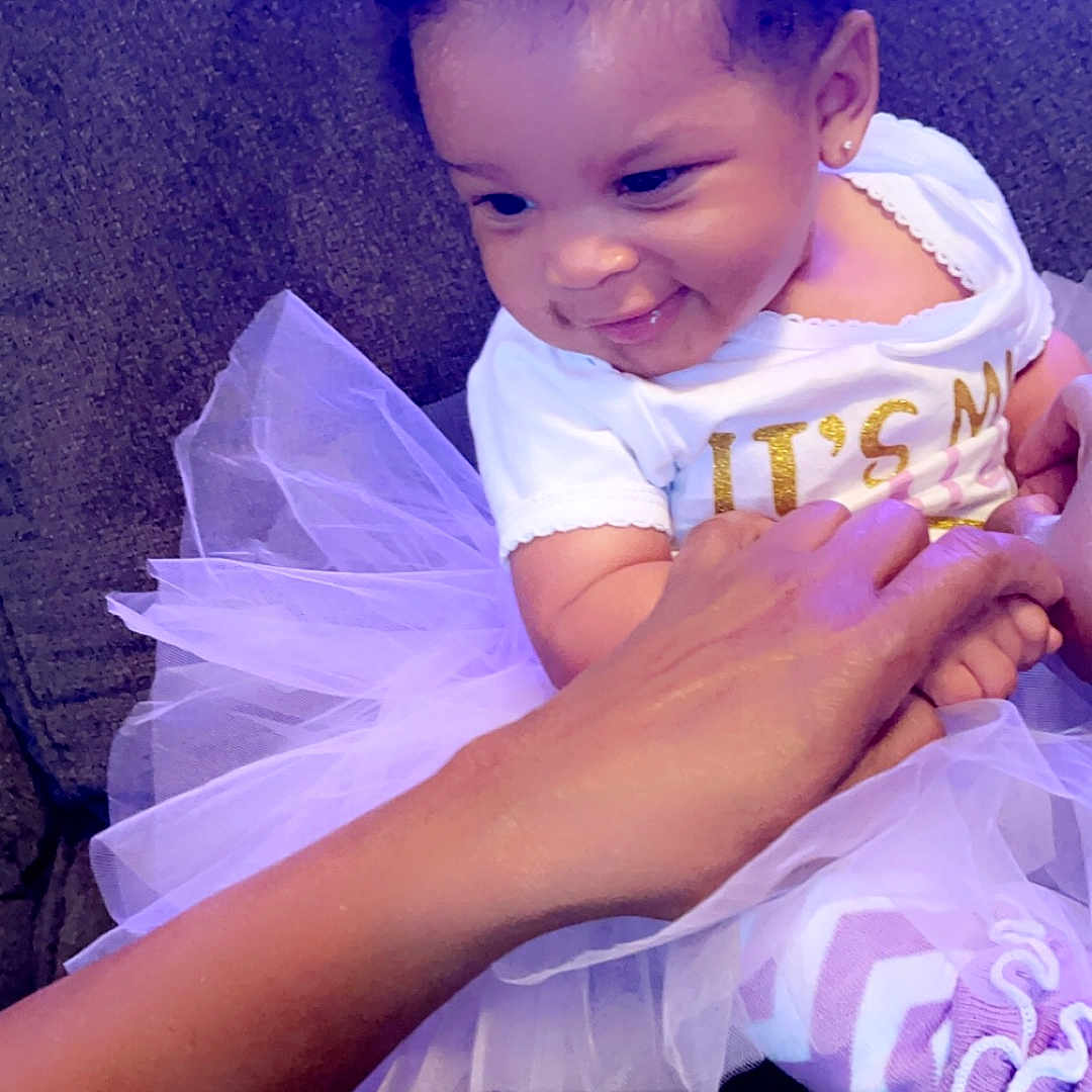 Tiana joined the competition — help win amazing prizes! accessories, baby, clothing, costume, couch, dress, face, fashion, formalwear, furniture, gown, hat, head, jewelry, person, photography, portrait, purple, sitting, tie