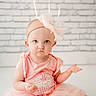 baby, child, girl, pink_dress, headband, bow, blue_eyes, cupcake_design, sitting, white_brick_wall, indoor, cute, portrait, infant, expression, curious, soft_lighting, young_child, tutu, fashion