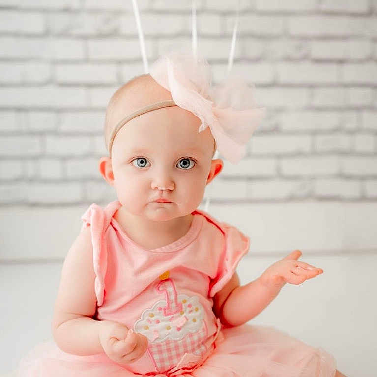 Maddy Huffman joined the competition — help win amazing prizes! baby, child, girl, pink_dress, headband, bow, blue_eyes, cupcake_design, sitting, white_brick_wall, indoor, cute, portrait, infant, expression, curious, soft_lighting, young_child, tutu, fashion