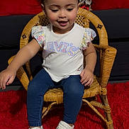 Ariadna is registered to the contest to win money with this photo: child, toddler, girl, sitting, portrait, smiling, happy, face, bows, hair_accessories, white_shirt, jeans, sneakers, rattan_chair, wicker_furniture, red_carpet, couch, indoor, fashion, photography