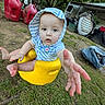 Kye is registered to the contest to win money with this photo: baby, child, hoodie, yellow_seat, outdoor, grass, tree, red_gas_cans, camping_gear, curious, reaching_hand, person, young_child, dirt_ground, greenery, daylight, casual_clothing, playful, nature, expression