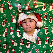 Cannon is registered to the contest to win money with this photo: celebration, child, christmas, curious, cute, face, festive, green, hat, holiday, holiday_season, indoors, portrait, red, santa_hat, snowman_pattern, toddler, white, winter, wrapping_paper