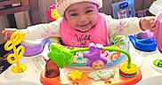 Vision is registered to the contest to win money with this photo: activity_center, baby, bib, carpet, child, colorful, family_photo, fisher_price, footwear, furniture, happy, hat, indoor, infant, knit_hat, person, playtime, purple_shoes, smiling, toy