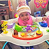 activity_center, baby, bib, carpet, child, colorful, family_photo, fisher_price, footwear, furniture, happy, hat, indoor, infant, knit_hat, person, playtime, purple_shoes, smiling, toy