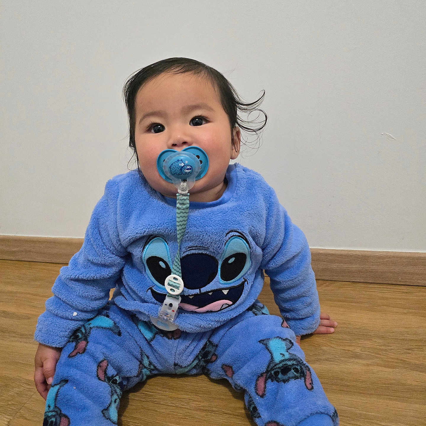 Keeran participe au concours pour gagner de l'argent avec cette photo : baby, blue_clothing, casual, child, comfort, cute, face, floor, foot, hair, hand, indoors, pacifier, pacifier_clip, pajamas, person, sitting, stitch, wall, wooden_floor