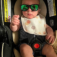 Harrison is registered to the contest to win money with this photo: baby, child, car_seat, sunglasses, bib, polka_dots, infant, seatbelt, reflection, serious_face, hand, clothing, indoor, cute, baby_boy, closeup, safety, accessory, portrait, seat