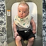 Harrison is registered to the contest to win money with this photo: baby, infant, child, bib, shorts, baby_seat, cushion, carpet, hair_spikes, indoor, person, cute, sitting, wide_eyes, expression, skin, legs, hands, footwear_absent, clothing