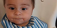 Levi is registered to the contest to win money with this photo: baby, child, high_chair, bib, striped_bib, food_on_face, cute, infant, indoor, person, portrait, feeding_time, curious, young_child, sitting, face, head, expression, clothing, closeup