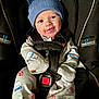 baby, infant, car_seat, blue_hat, onesie, smiling, cute, child, safety_harness, black_car_seat, patterned_clothing, happy, indoors, seatbelt, small_child, adorable, playful, headwear, baby_clothes, toddler