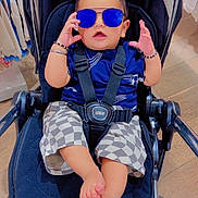 Mehtab Singh is registered to the contest to win money with this photo: baby, child, stroller, sunglasses, blue_sunglasses, checkered_shorts, bracelet, footwear_free, indoor, shopping, clothing_rack, floor, wood_floor, person, cute, fashion, baby_clothes, seat_belt, casual, accessory