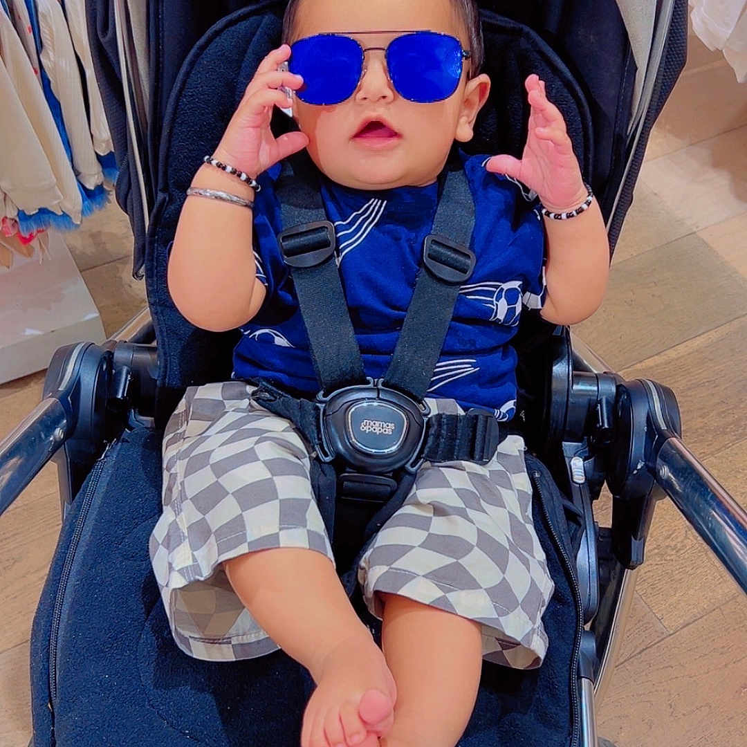Mehtab Singh is registered to the contest to win money with this photo: accessory, baby, baby_clothes, blue_sunglasses, bracelet, casual, checkered_shorts, child, clothing_rack, cute, fashion, floor, footwear_free, indoor, person, seat_belt, shopping, stroller, sunglasses, wood_floor