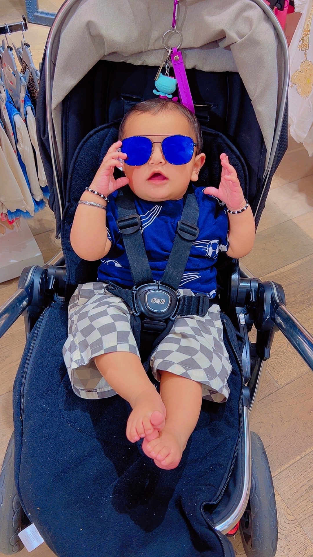 Mehtab Singh is registered to the contest to win money with this photo: baby, child, stroller, sunglasses, blue_sunglasses, checkered_shorts, bracelet, footwear_free, indoor, shopping, clothing_rack, floor, wood_floor, person, cute, fashion, baby_clothes, seat_belt, casual, accessory