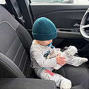 Liam participe au concours pour gagner de l'argent avec cette photo : child, infant, baby, beanie, hat, pacifier, water_bottle, plush_toy, car_interior, car_seat, seatbelt, armrest, steering_wheel, window, gray_clothing, sitting, passenger, toddler, cozy_outfit, front_seat