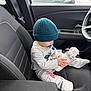 child, infant, baby, beanie, hat, pacifier, water_bottle, plush_toy, car_interior, car_seat, seatbelt, armrest, steering_wheel, window, gray_clothing, sitting, passenger, toddler, cozy_outfit, front_seat