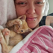 Gizzmo is registered to the contest to win money with this photo: animal, blanket, cat, close_up, comfort, cozy, cute, face, feline, indoor, kitten, orange, person, pet, pink, relaxed, resting, sleepy, snuggling, soft