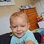 toddler, smiling, child, indoor, toys, dresser, television, blue_shirt, person, face, happy, room, furniture, light, skin, hair, floor, clothing, hand, baby