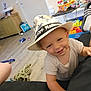 Leo participe au concours pour gagner de l'argent avec cette photo : toddler, child, hat, smile, indoor, toy, floor, wooden_floor, living_room, furniture, colorful, play, happy, person, baby, clothing, footwear, couch, cabinet, casual