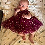 Hadley is registered to the contest to win money with this photo: baby, infant, dress, maroon, sparkly, blanket, floral_pattern, cute, lying_down, small_hands, bare_feet, indoors, child, person, portrait, fabric, soft, adorable, young, smiling