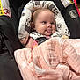baby, infant, car_seat, blanket, tongue_out, cute, child, seatbelt, patterned_fabric, pink, black, white, face, head, clothing, sitting, expression, indoor, soft, comfort