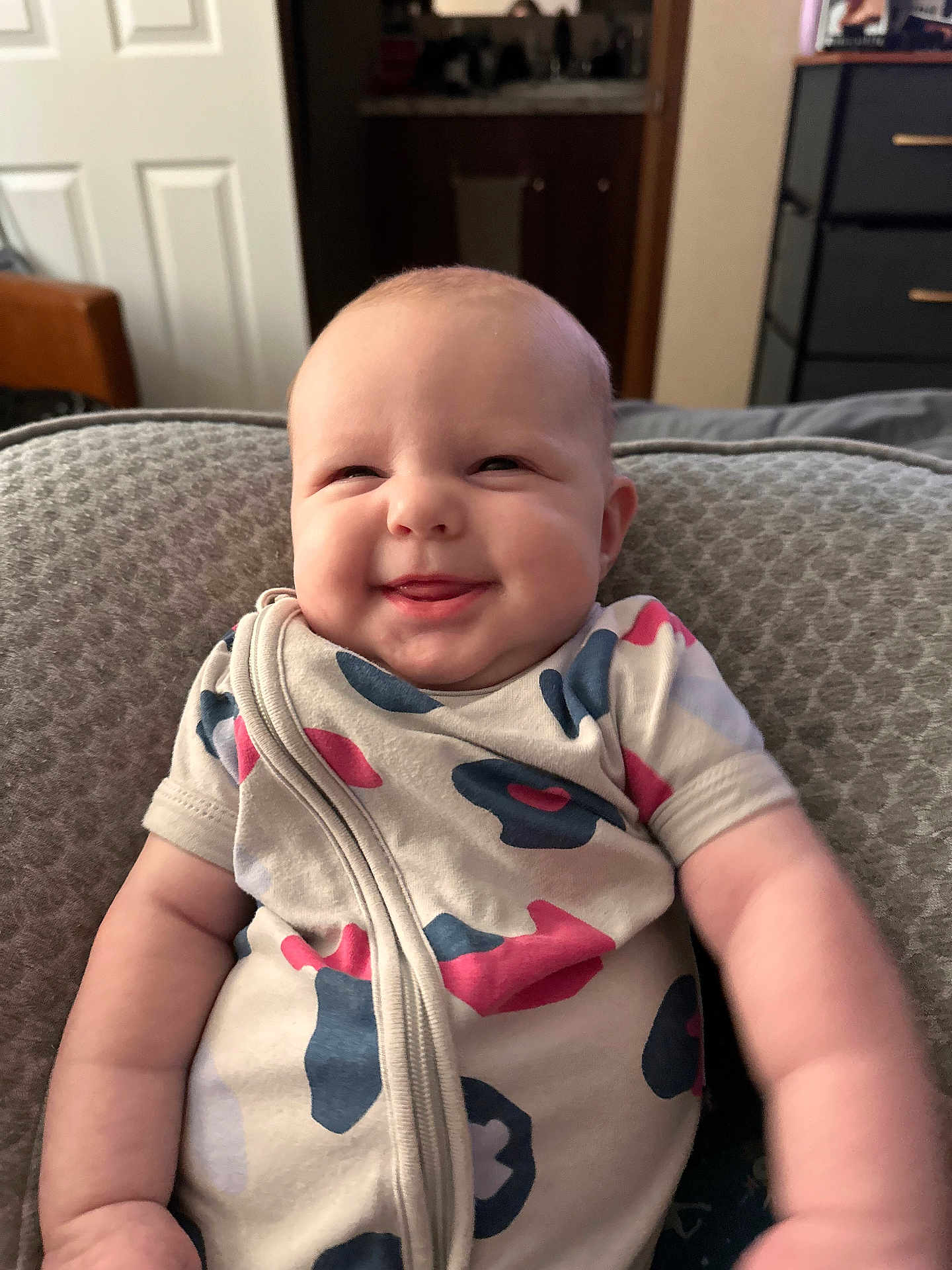 Hadley joined the competition — help win amazing prizes! baby, smiling, infant, onesie, cushion, indoor, face, cheeks, happy, child, person, clothing, seated, tongue_out, cute, plush, comfortable, young_child, portrait, home